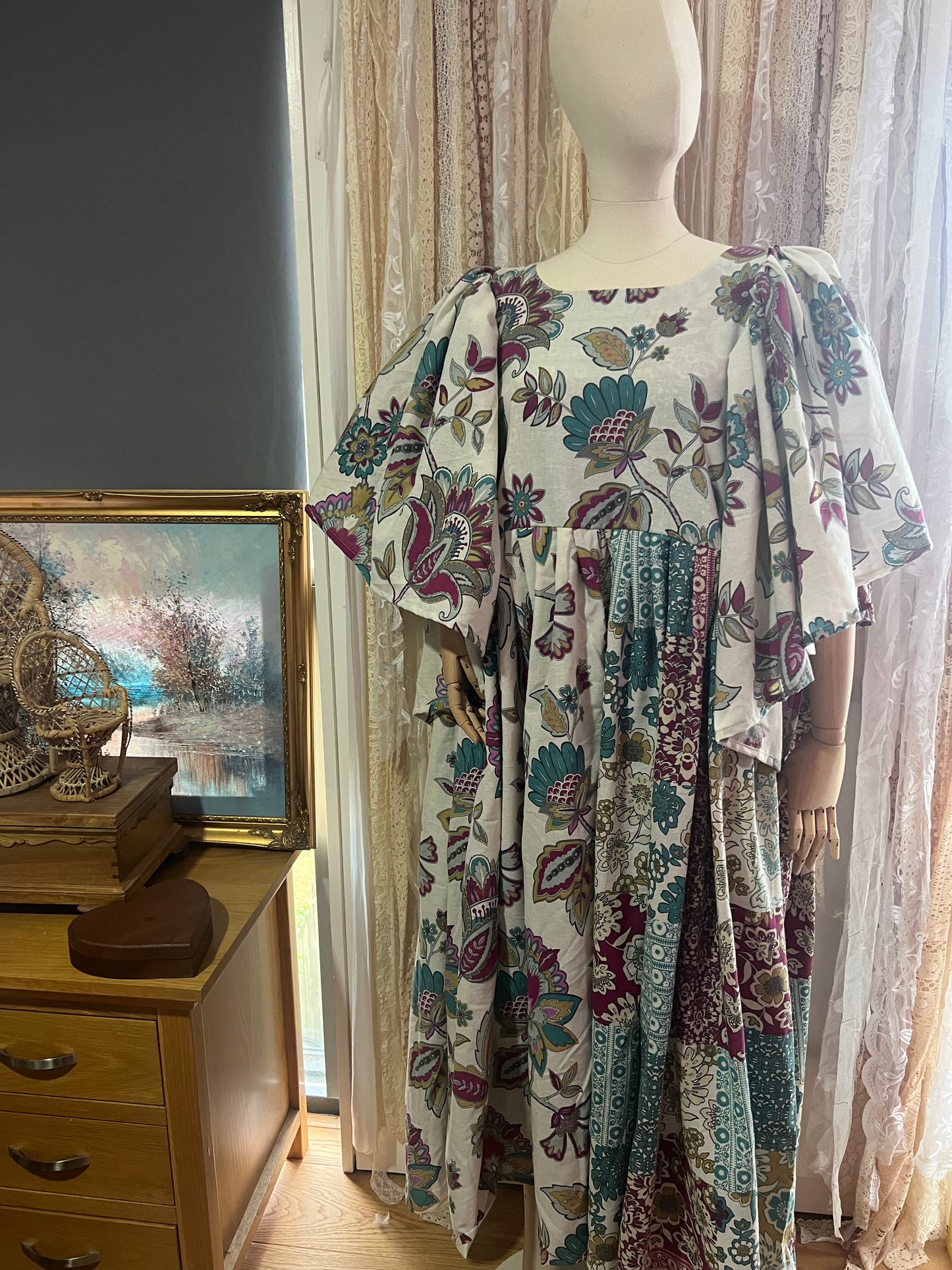 Mannequin wearing a floral dress in a room with a painting and wooden dresser.