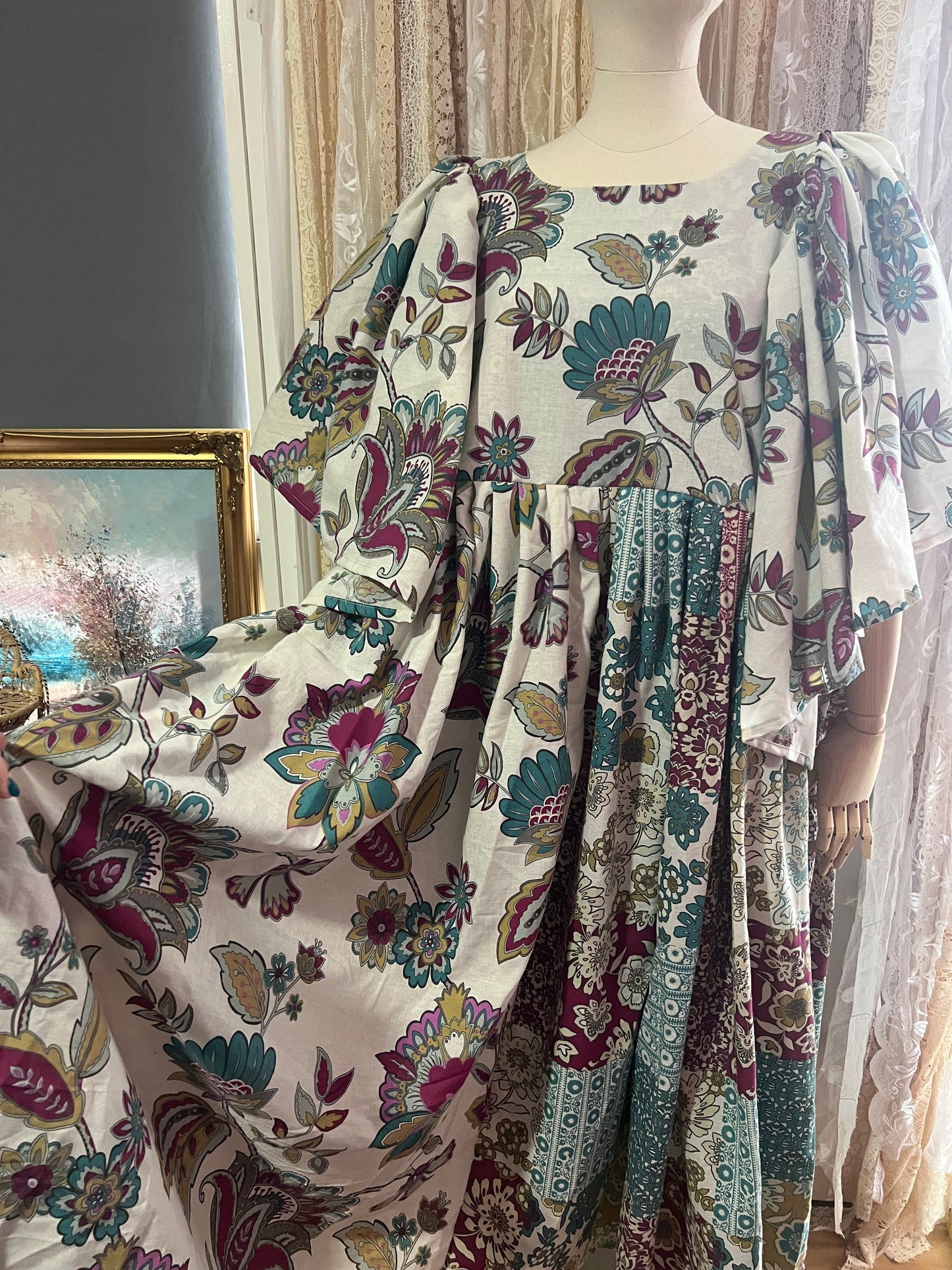 Mannequin wearing a floral dress with a decorative fabric draped over it, against a neutral background.
