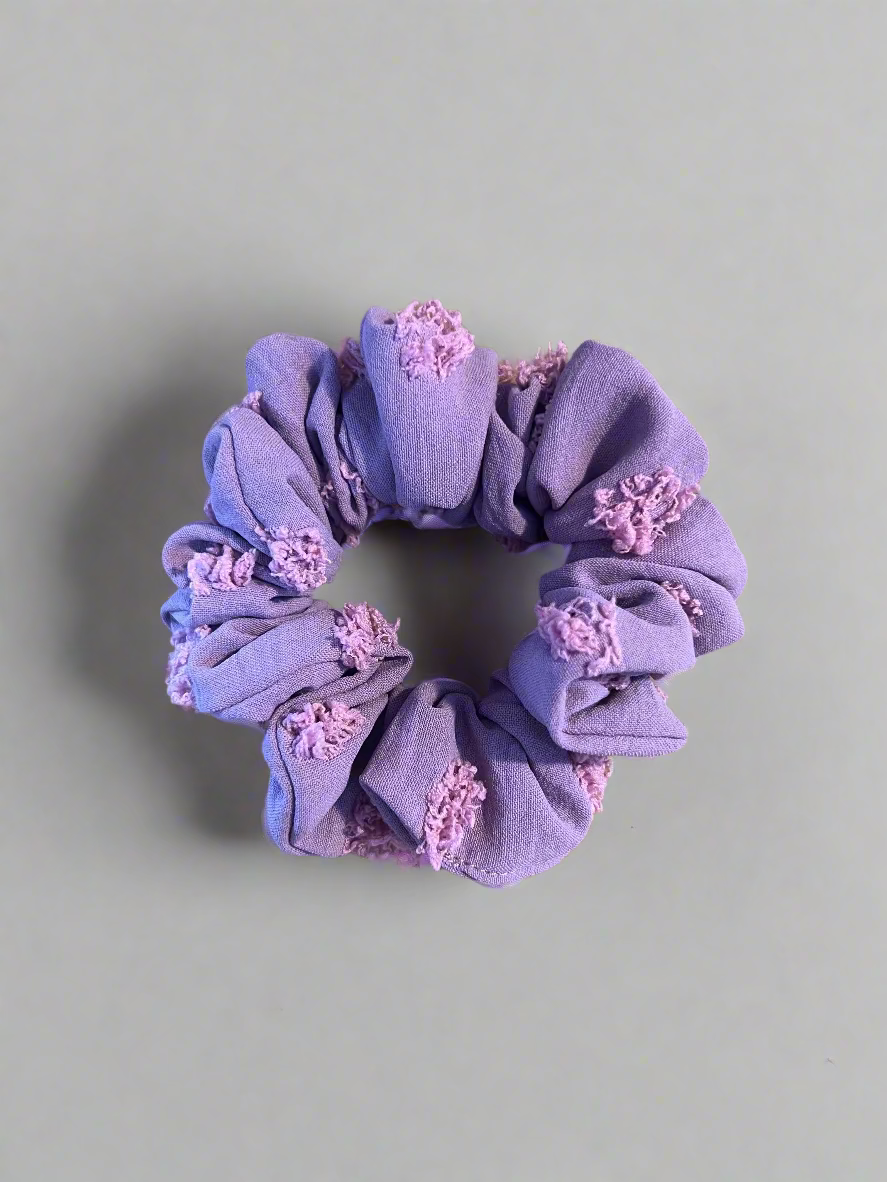 Purple scrunchie with floral designs on a wooden surface