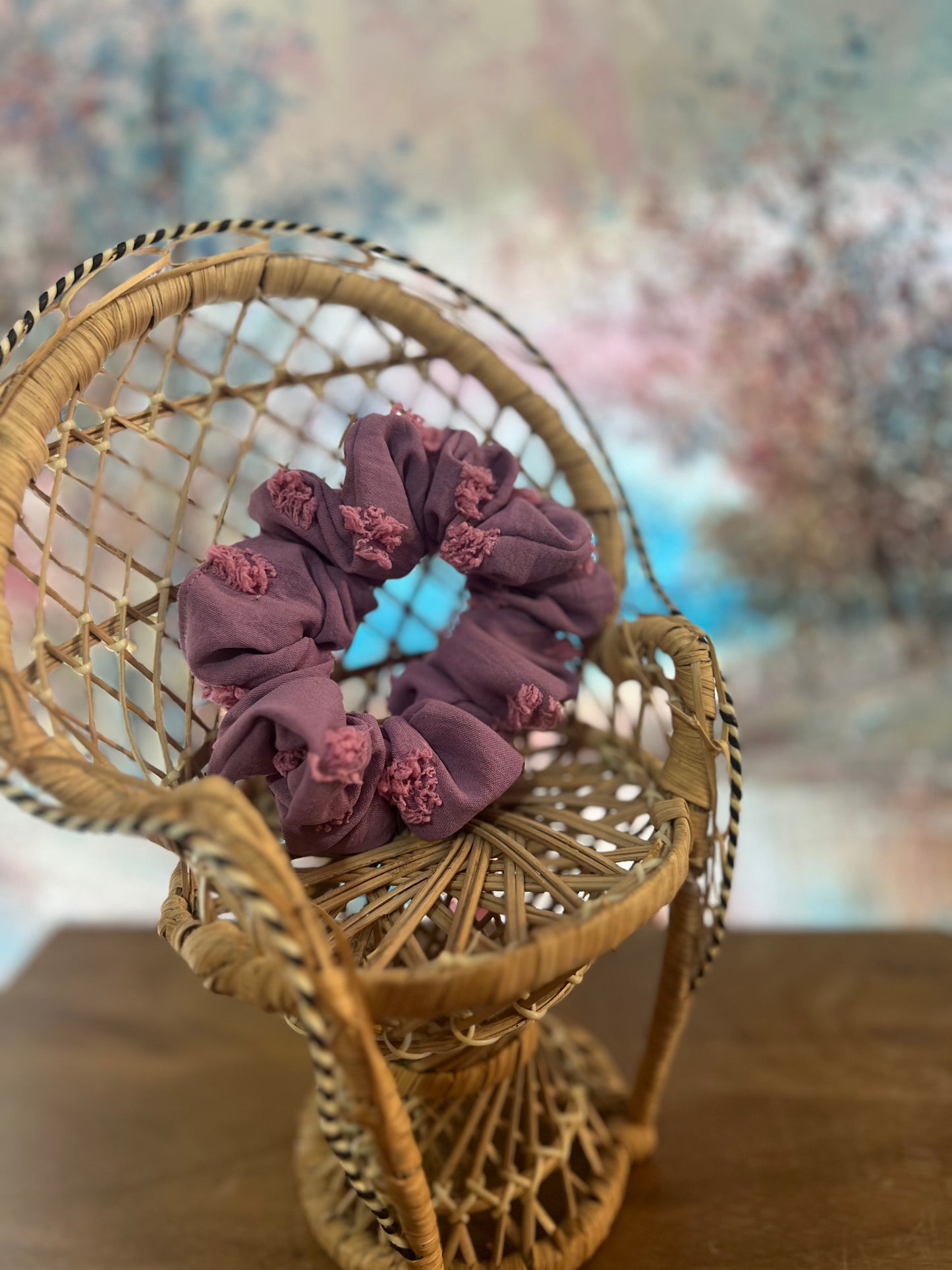 Purple scrunchie on a small wicker chair with a blurred floral background