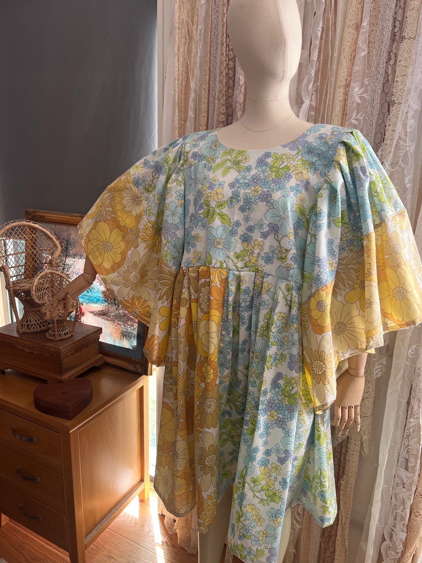 Floral dress on a mannequin in a room with curtains and furniture.