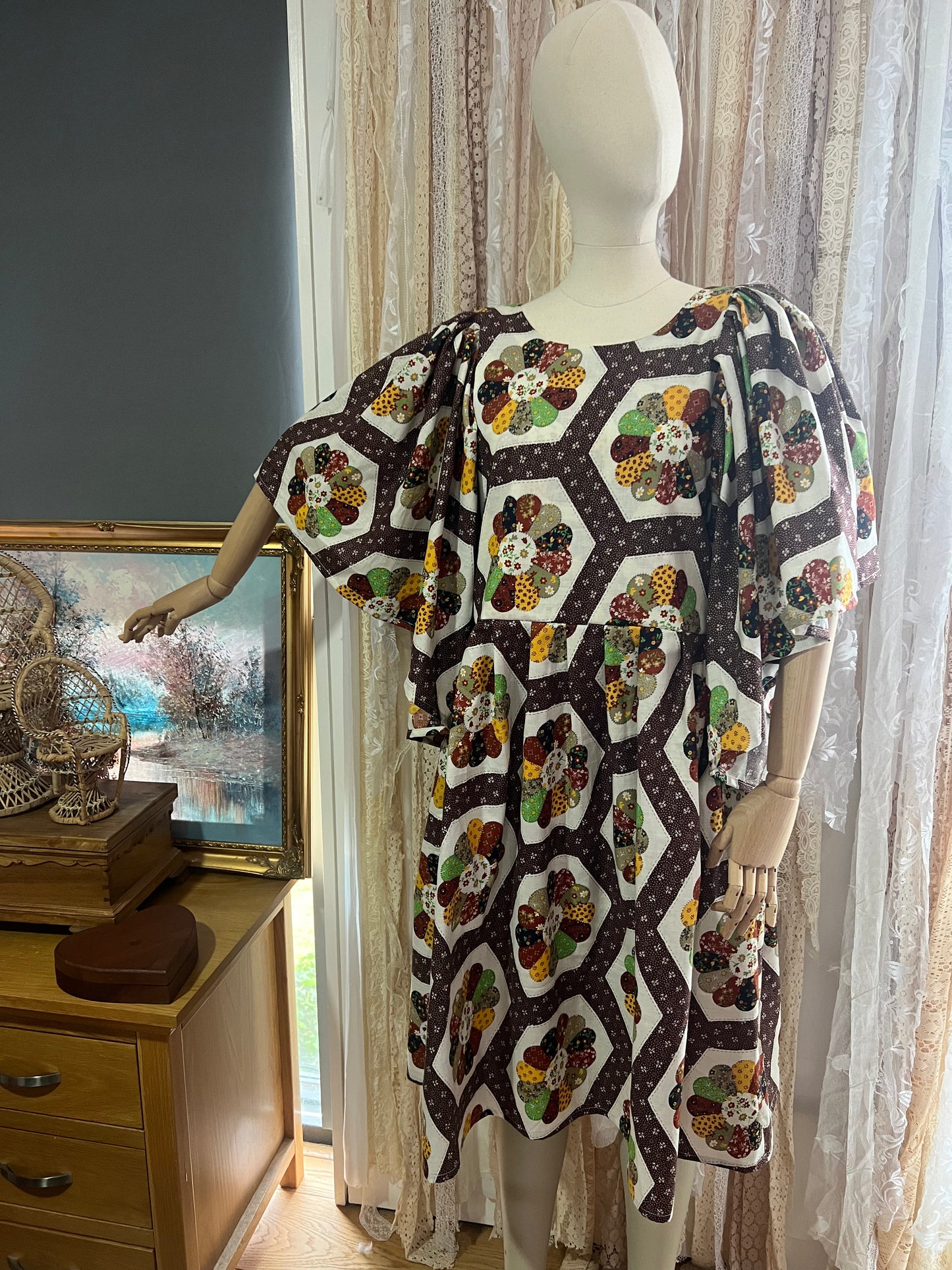 Mannequin wearing a patterned dress in a room with curtains and a painting.