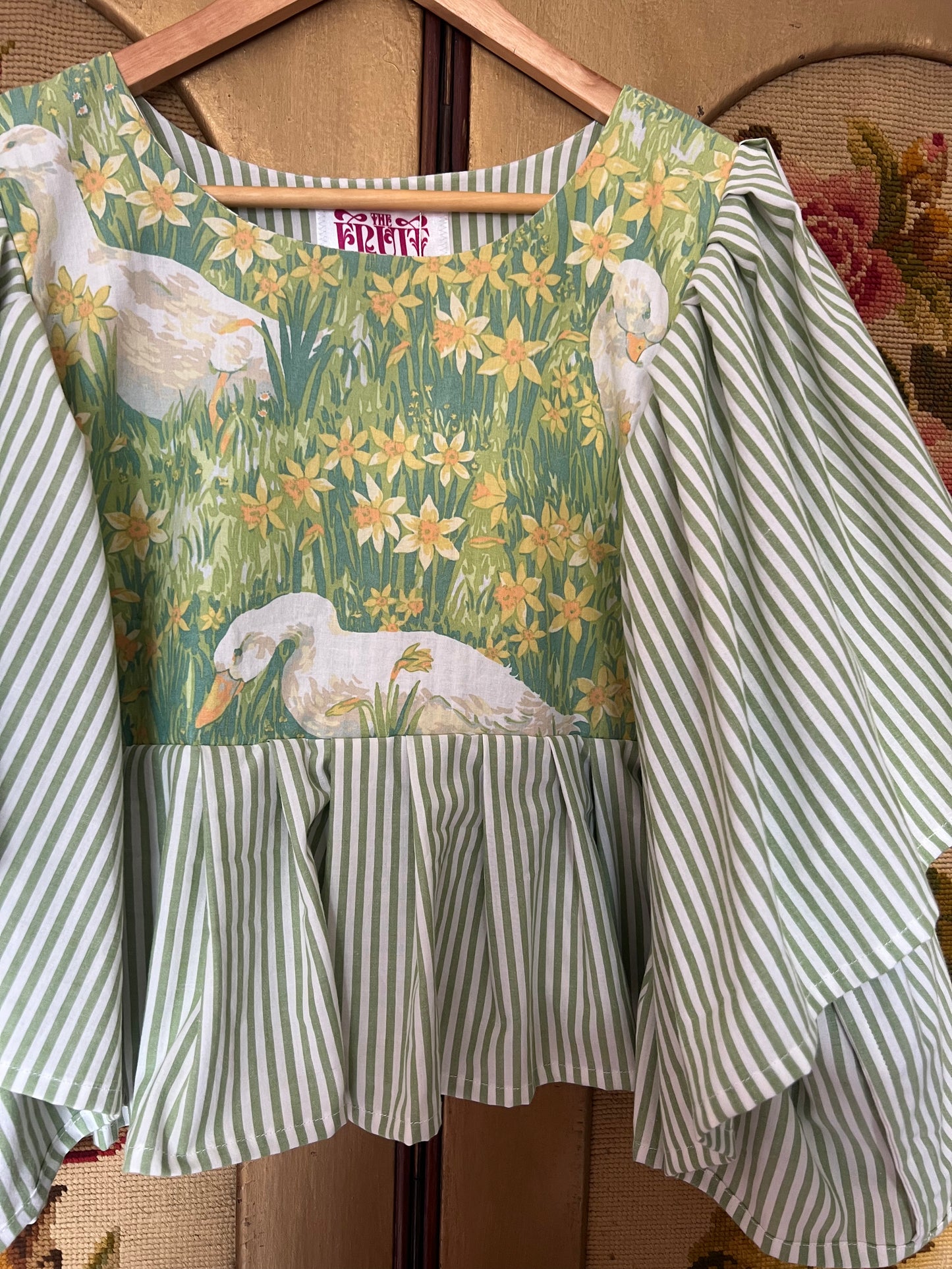 Green top with goose design and striped sleeves on a hanger