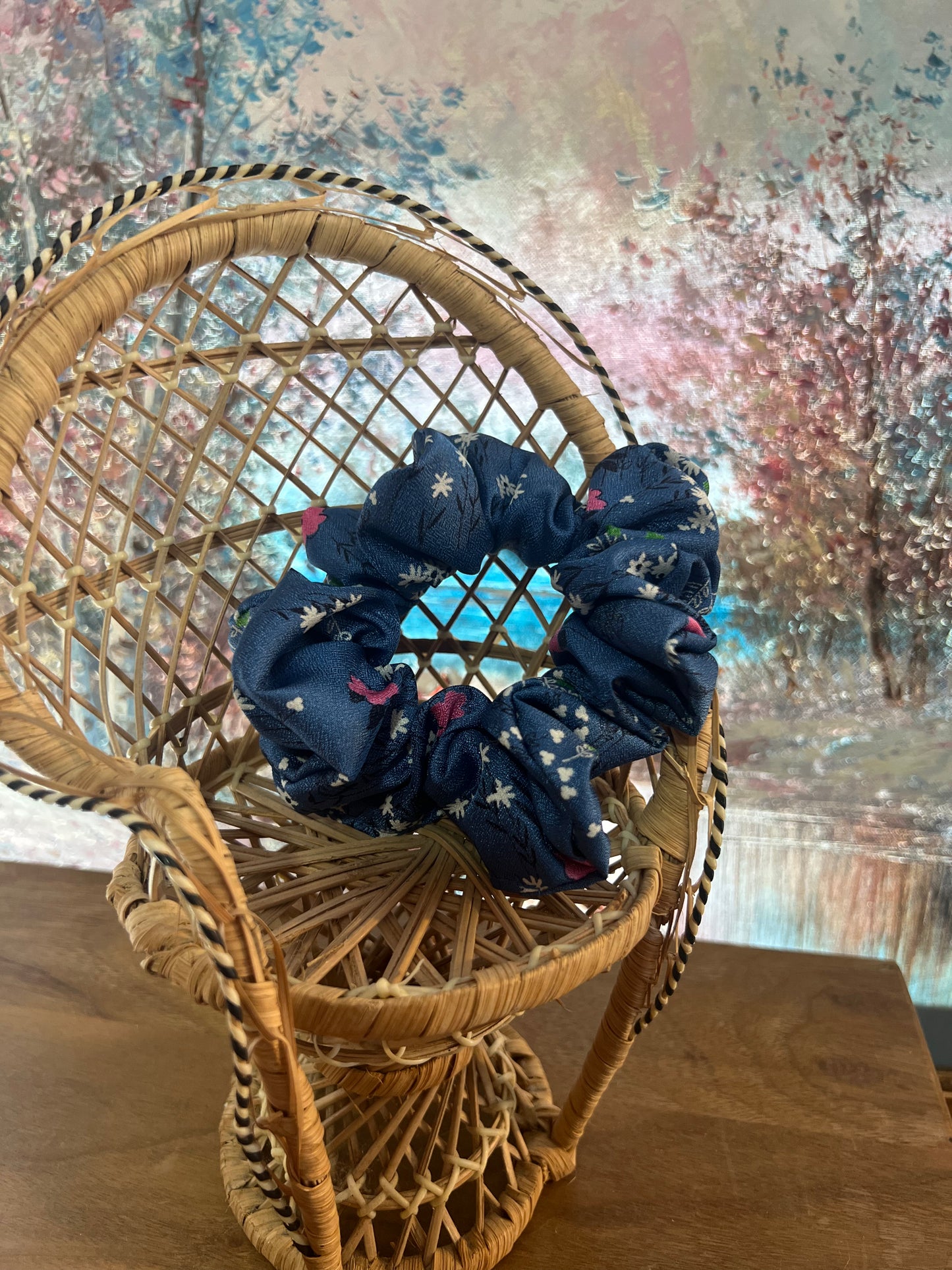 Navy blue scrunchies with floral patterns on a wicker chair against a textured wall.
