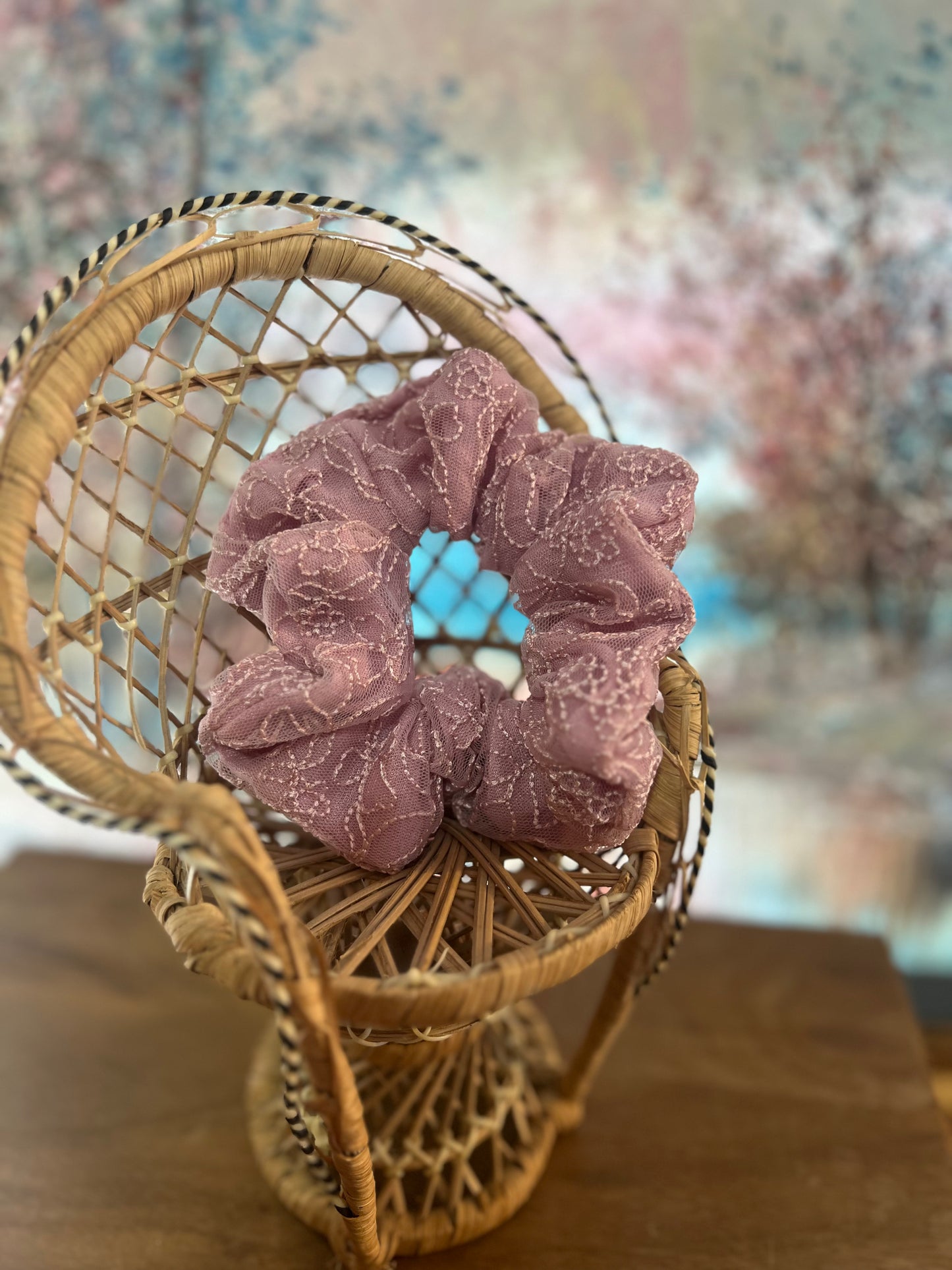 Pink scrunchie on a small wicker chair with a blurred floral background