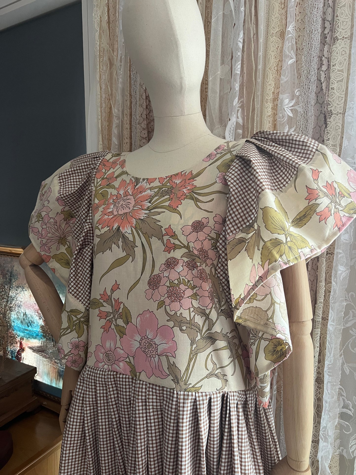 Mannequin wearing a floral dress with checkered sleeves and bottom, against a curtain background.
