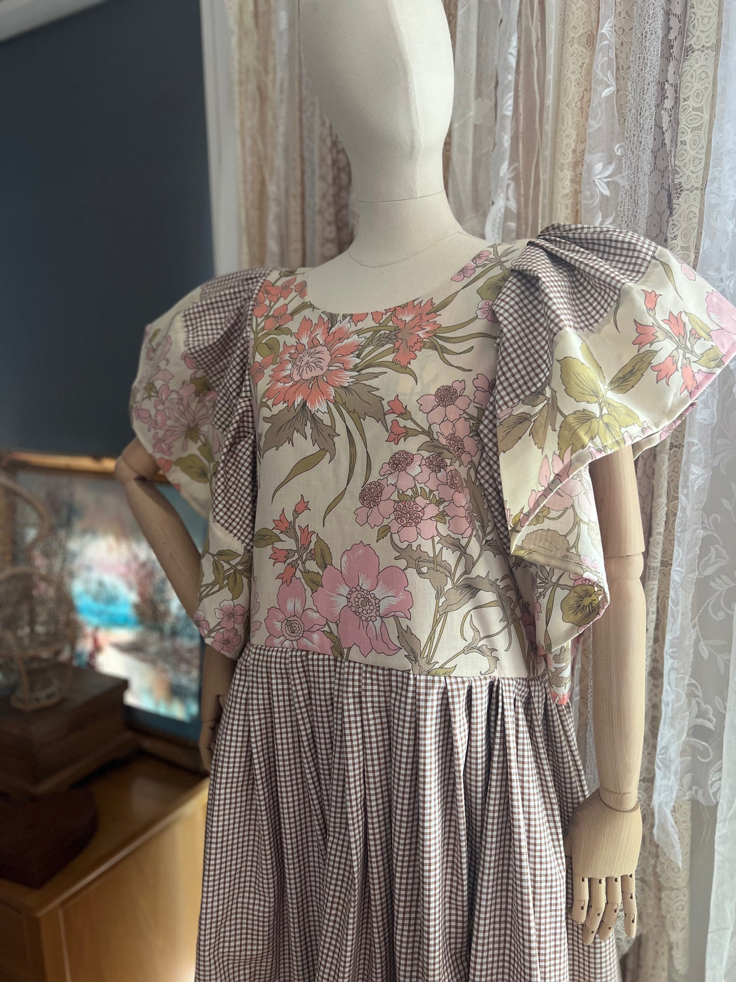 Mannequin wearing a floral dress with a checkered pattern in a room setting.