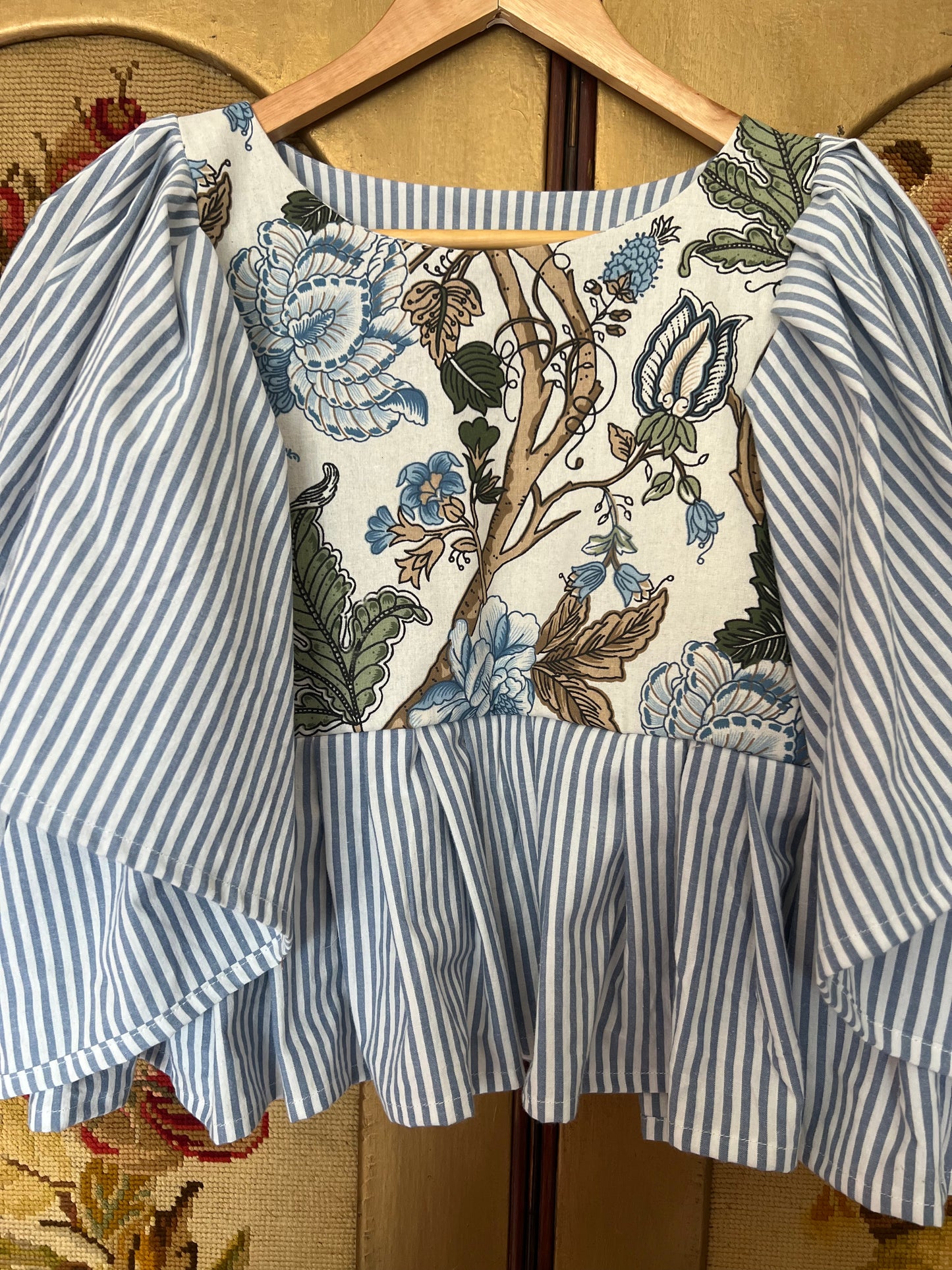 Striped blouse with floral pattern on a hanger against a decorative background