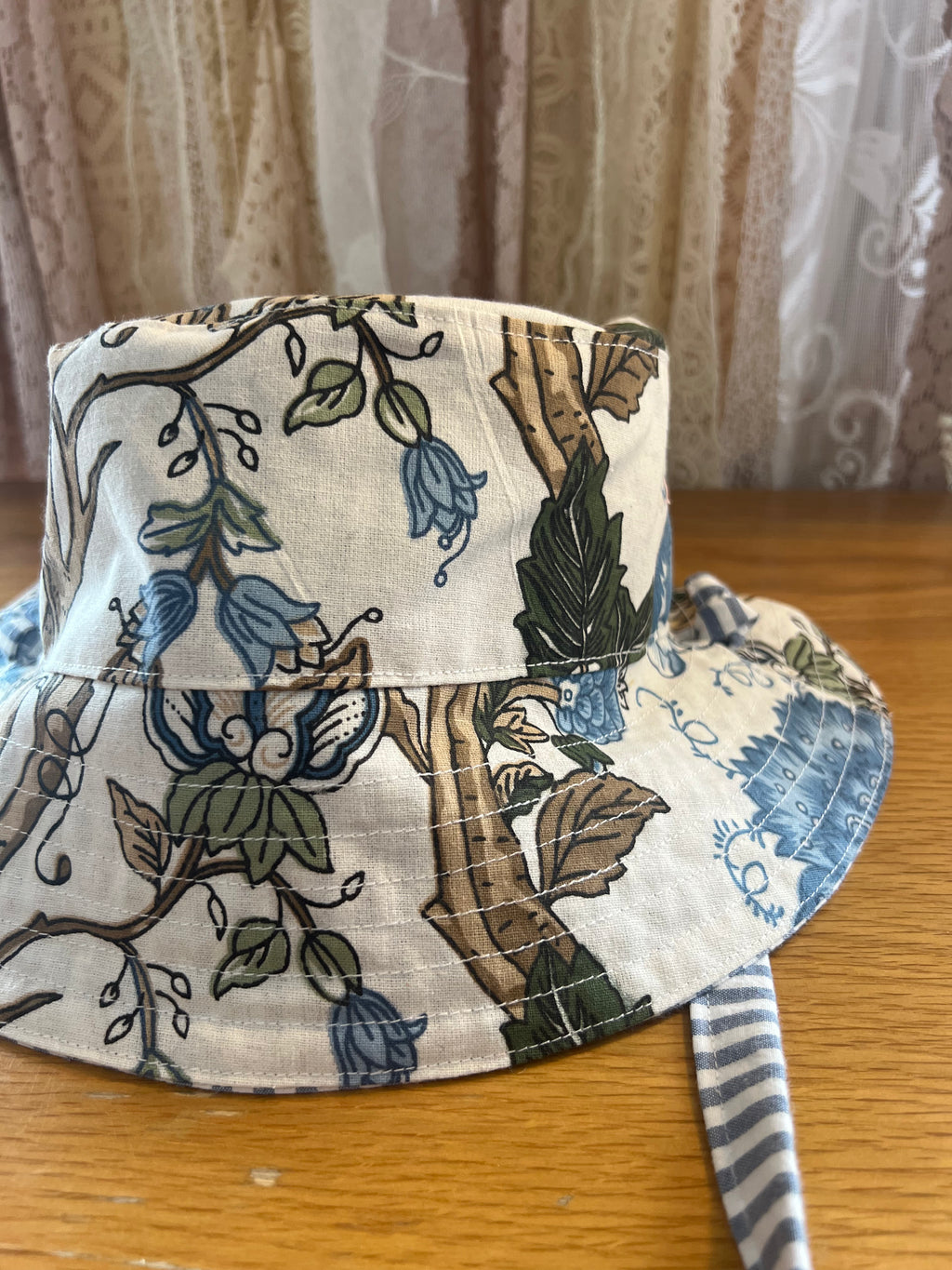 Floral-patterned bucket hat on a wooden surface with a curtain background