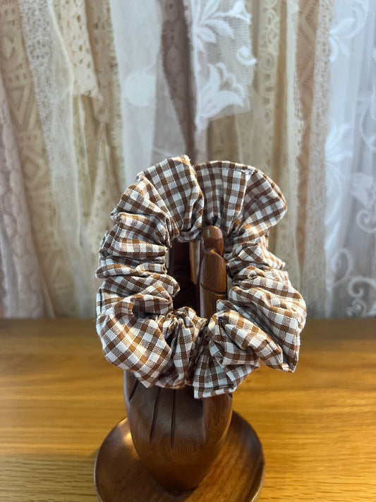 Brown checkered scrunchie on a wooden holder with a lace curtain background