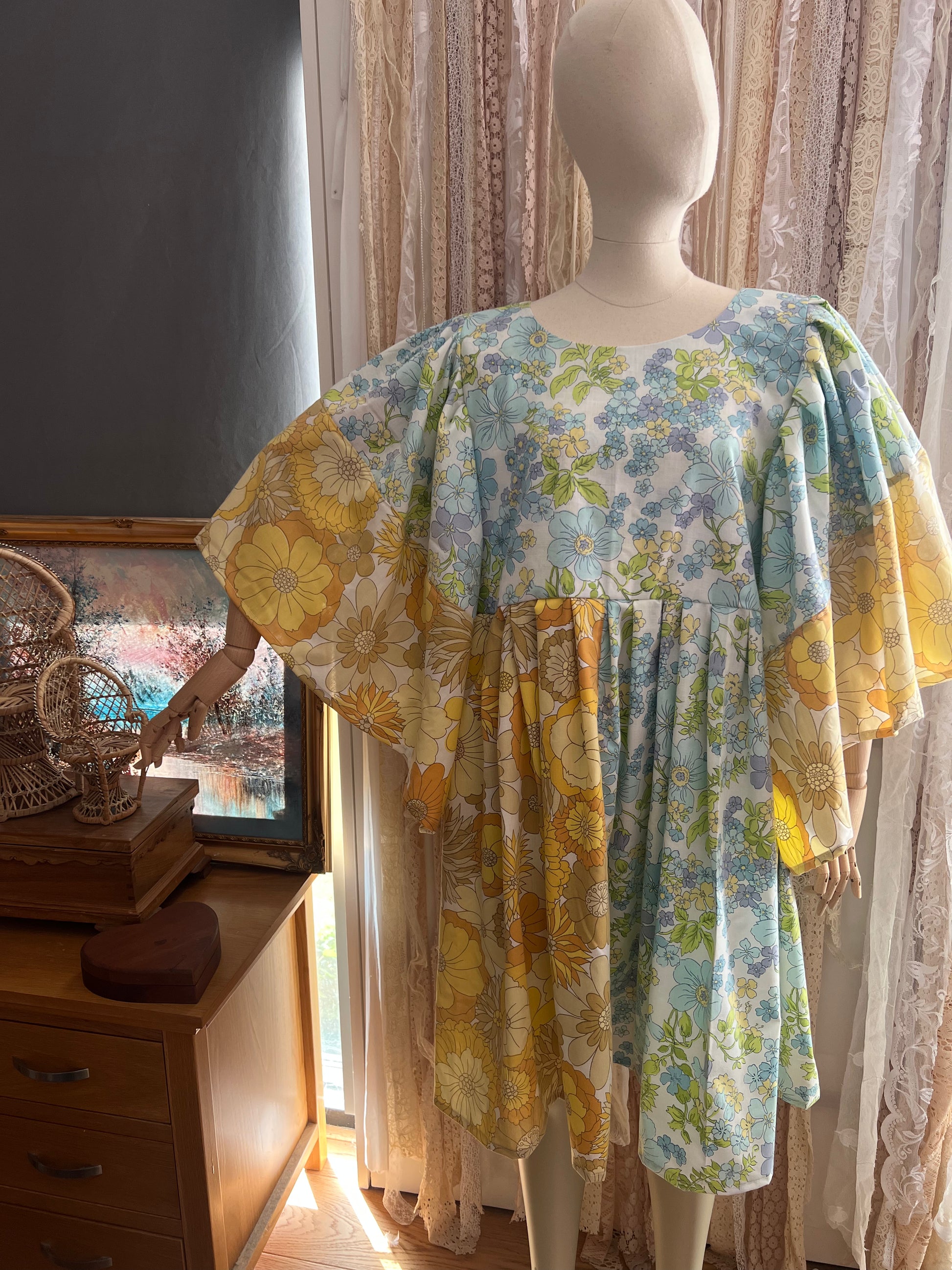 Mannequin wearing a floral dress in a room with curtains and a dresser.