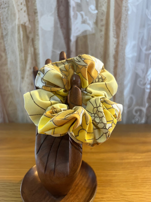 Yellow patterned scrunchie on a wooden holder against a lace curtain background