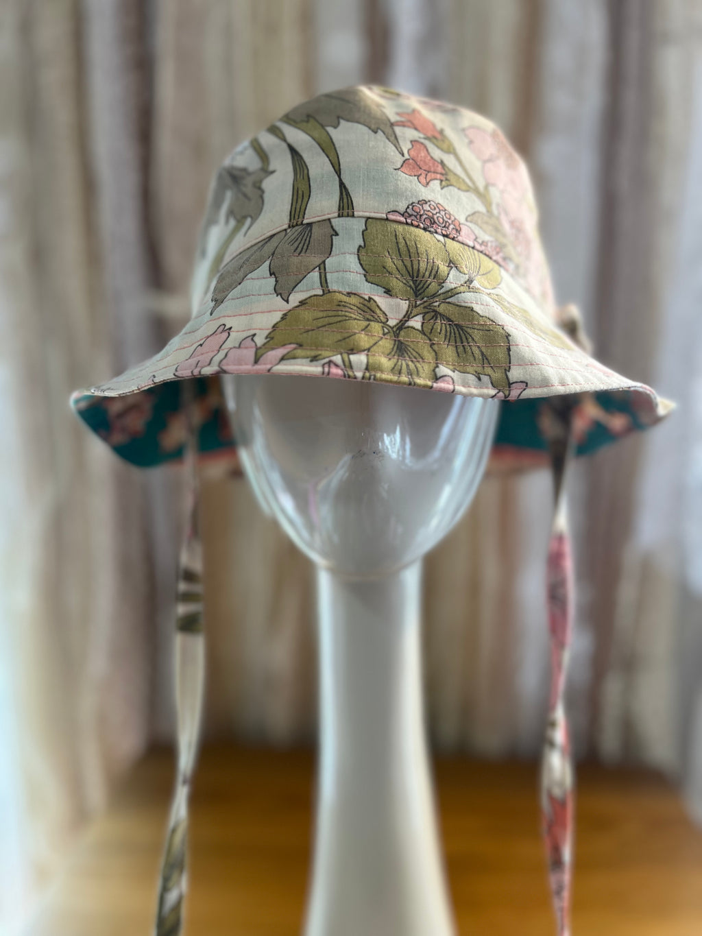 Floral-patterned bucket hat on a mannequin head with a blurred curtain background