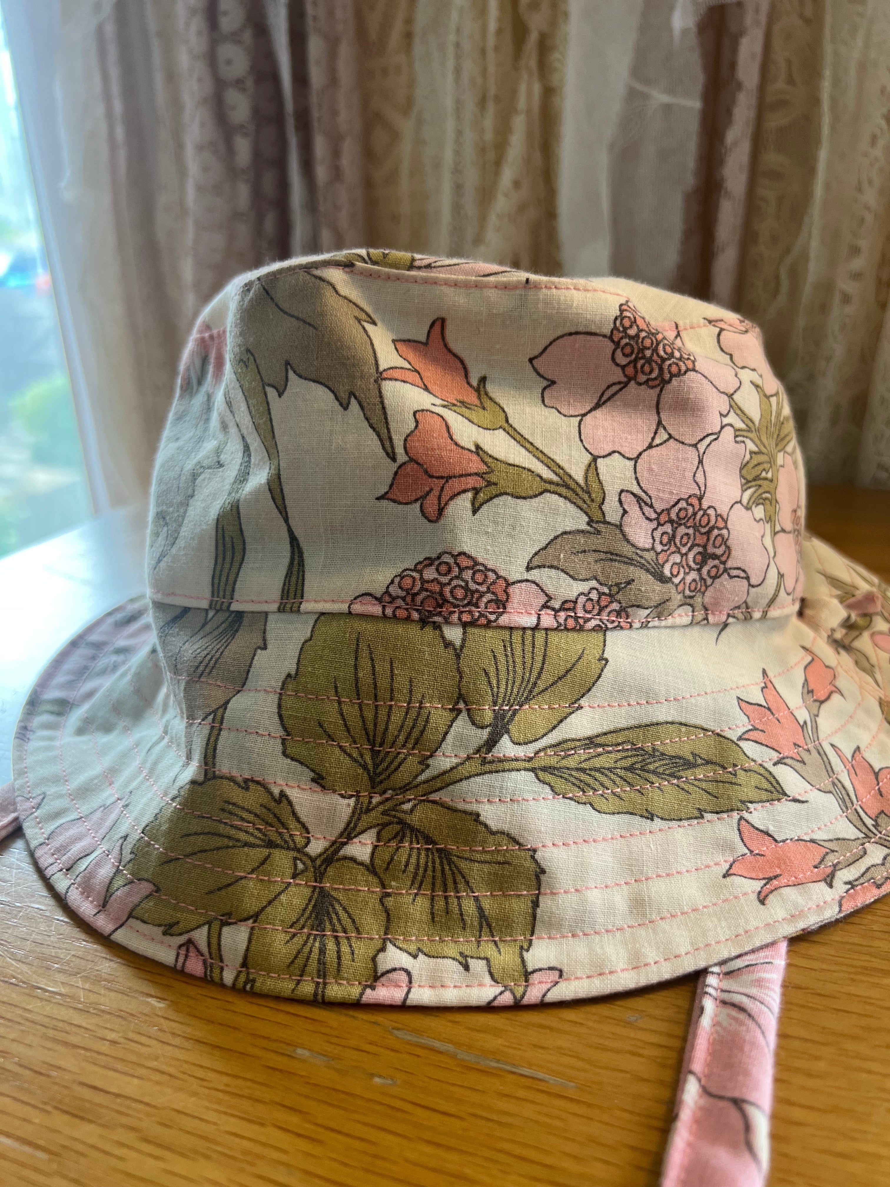 Floral-patterned bucket hat on a wooden surface with curtains in the background