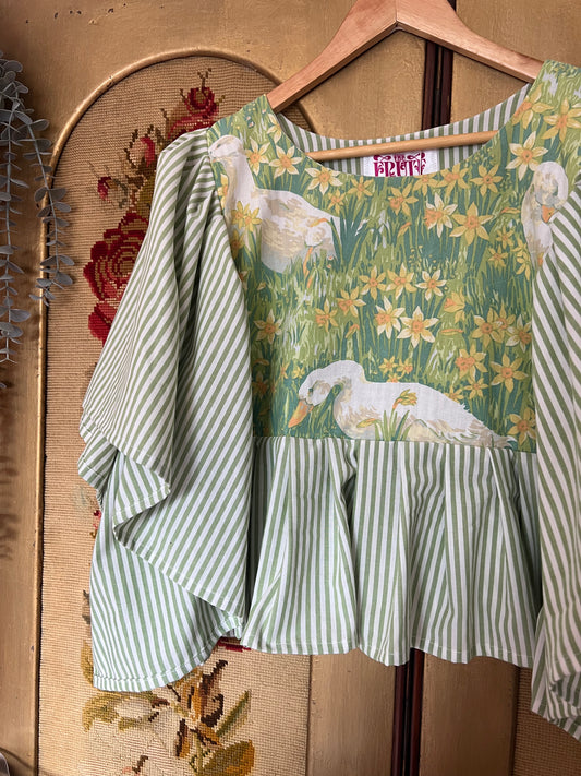 Green and white striped top with floral and bird pattern on a wooden hanger against a textured beige background.