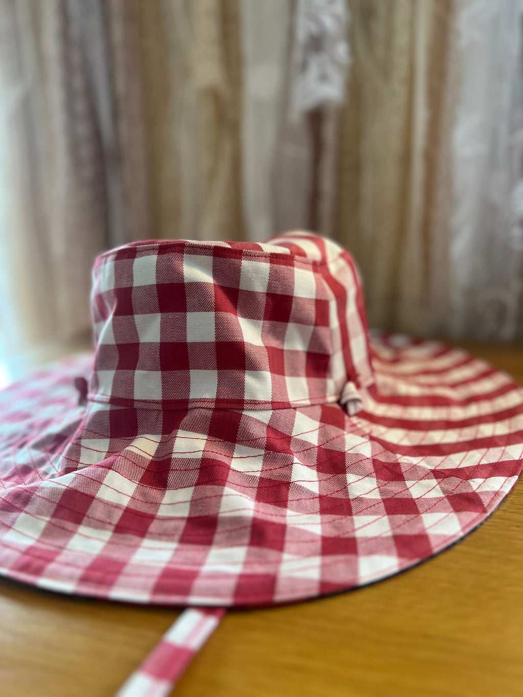 Red and white checkered hat on a wooden surface with a blurred curtain background