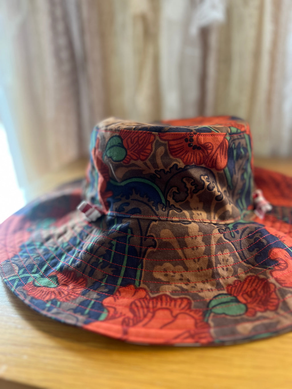 Colorful patterned bucket hat on a wooden surface with a blurred curtain background