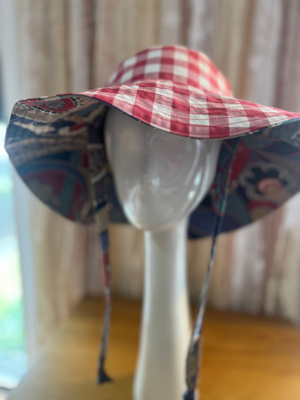 Mannequin head wearing a red and white checkered sun hat with colorful fabric brim.