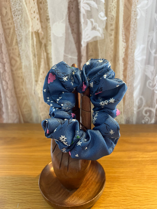 Blue floral scrunchies on a wooden stand with a lace curtain background
