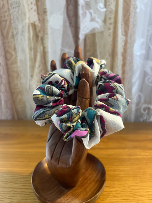 Colorful scrunchies on a wooden holder against a neutral background