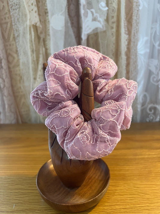 Pink lace scrunchie on a wooden holder with a lace curtain background