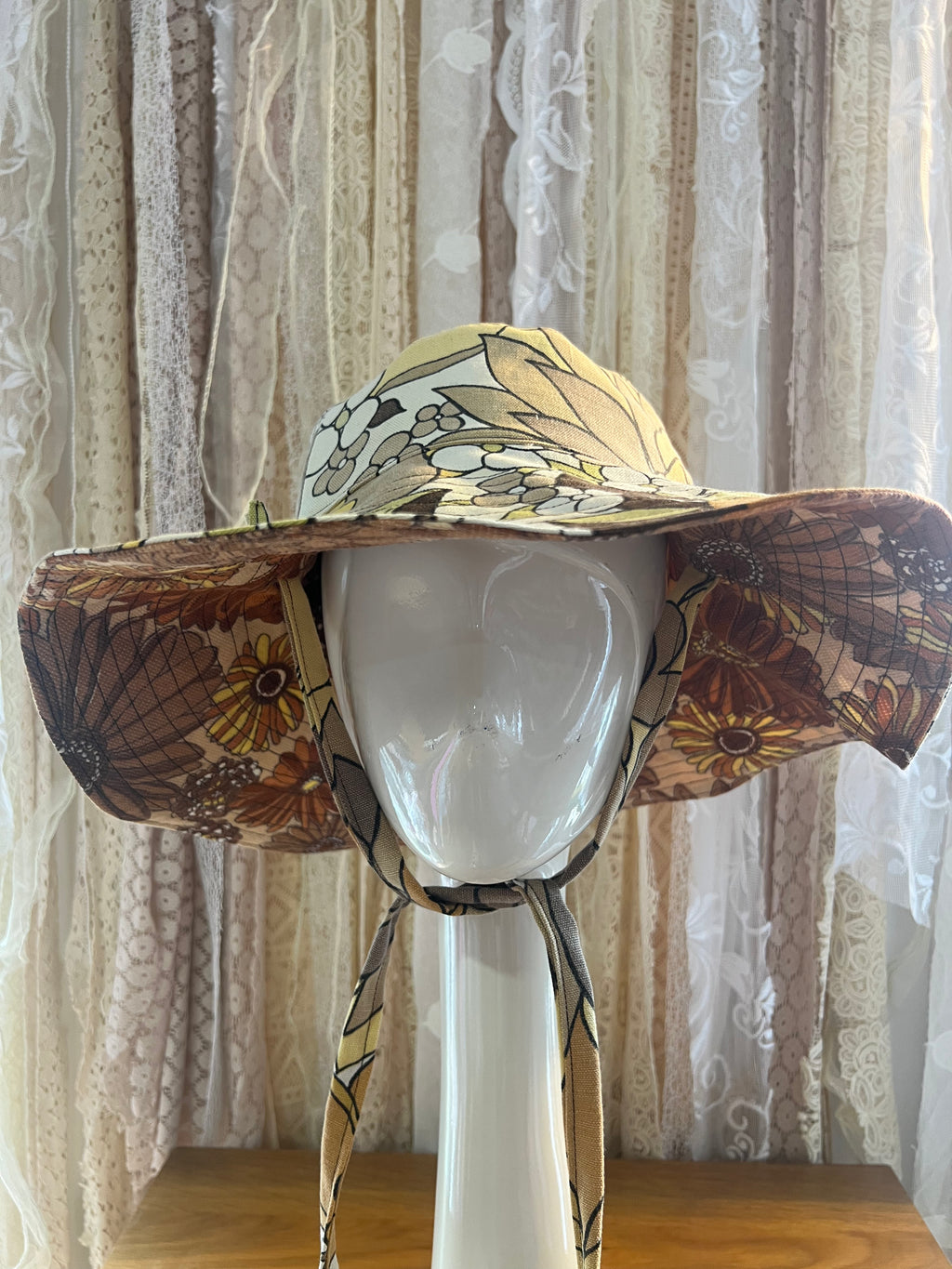 Floral-patterned sun hat on a mannequin head against a textured curtain background