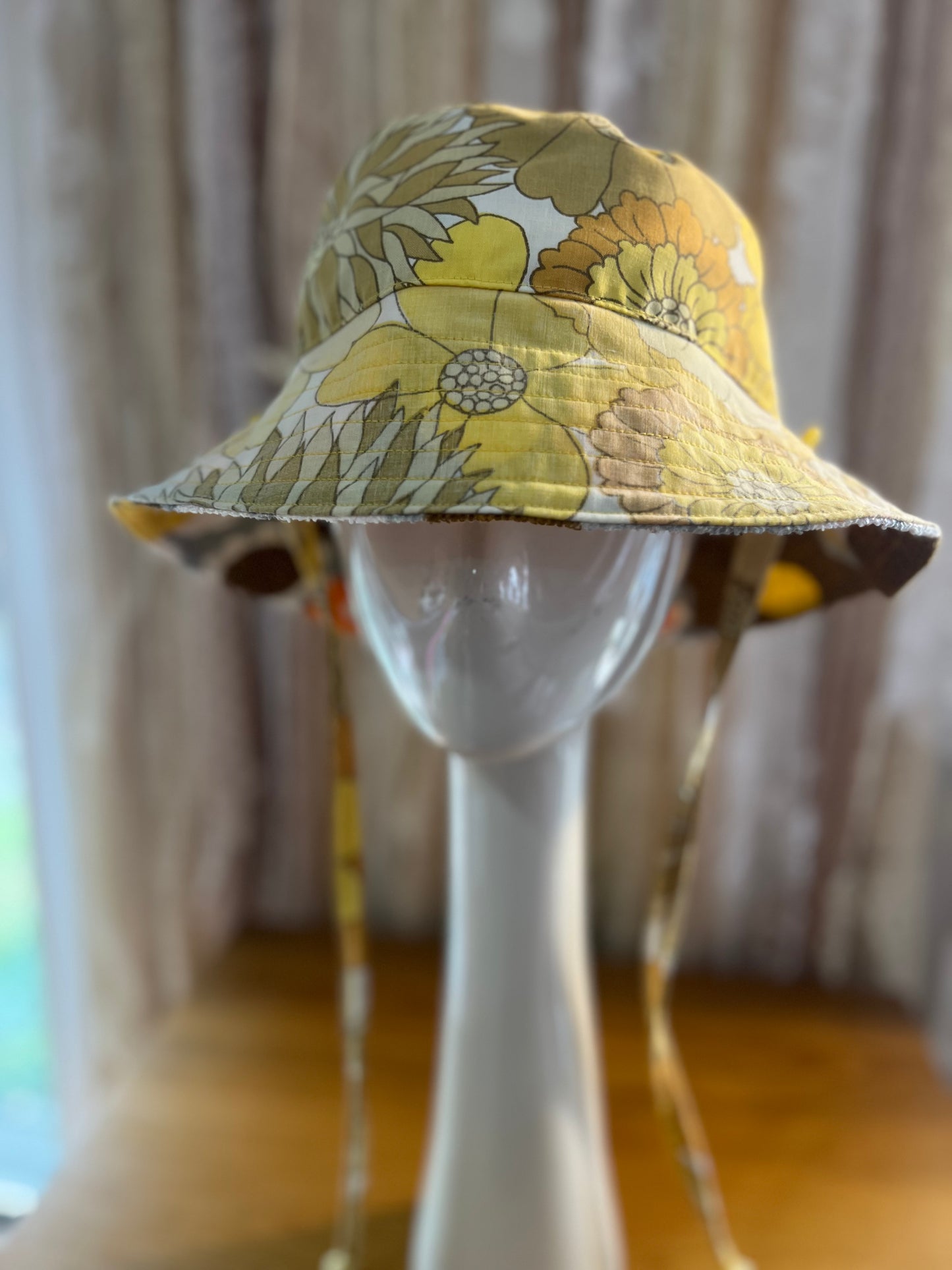Yellow floral bucket hat on a mannequin head with a blurred curtain background