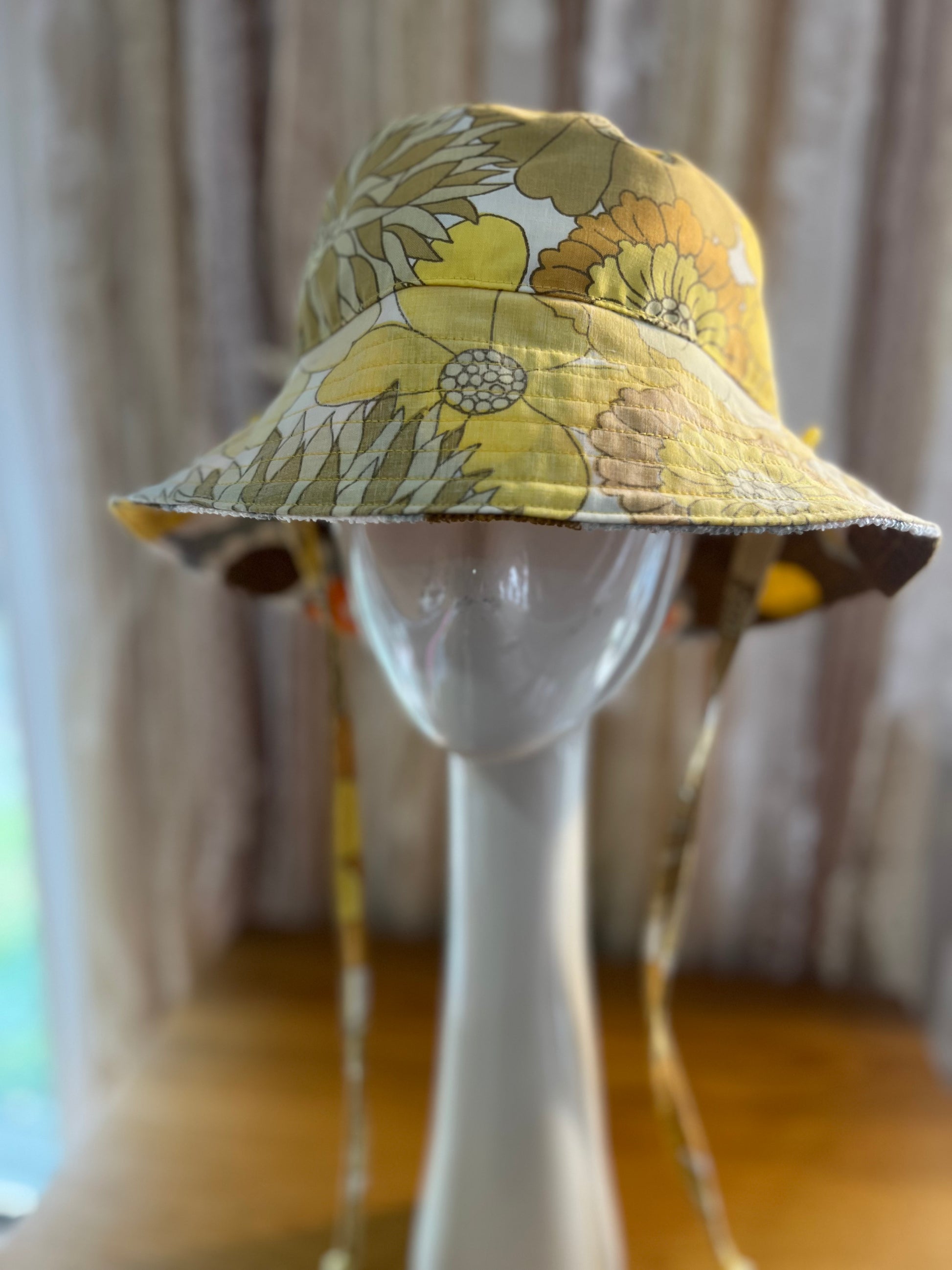 Yellow floral bucket hat on a mannequin head with a blurred curtain background