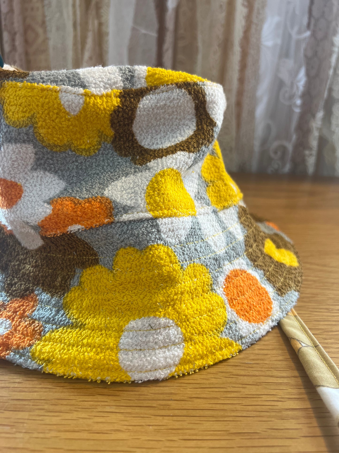 Floral-patterned hat on a wooden surface with a curtain in the background