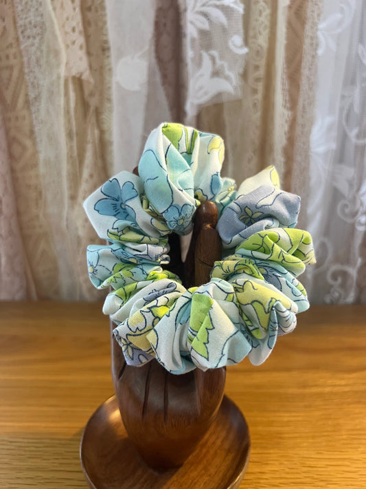 Floral patterned scrunchies on a wooden stand with a lace curtain background