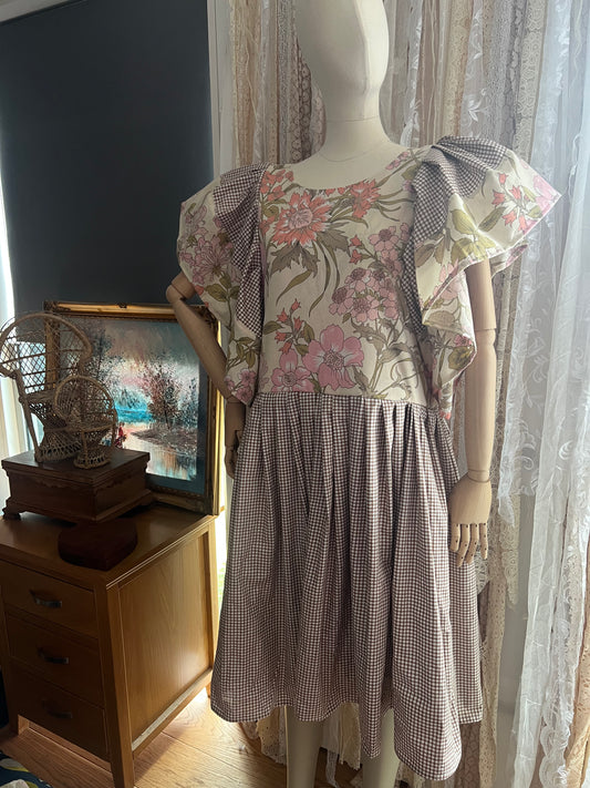 Mannequin wearing a floral dress with a checkered skirt in a room setting.